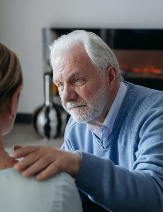 Elderly man placing a comforting hand on a caregiver's shoulder